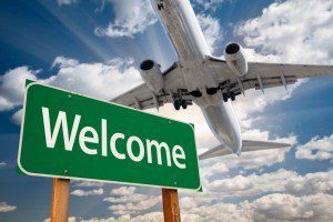 Welcome Green Road Sign and Airplane Above with Dramatic Blue Sky and Clouds.